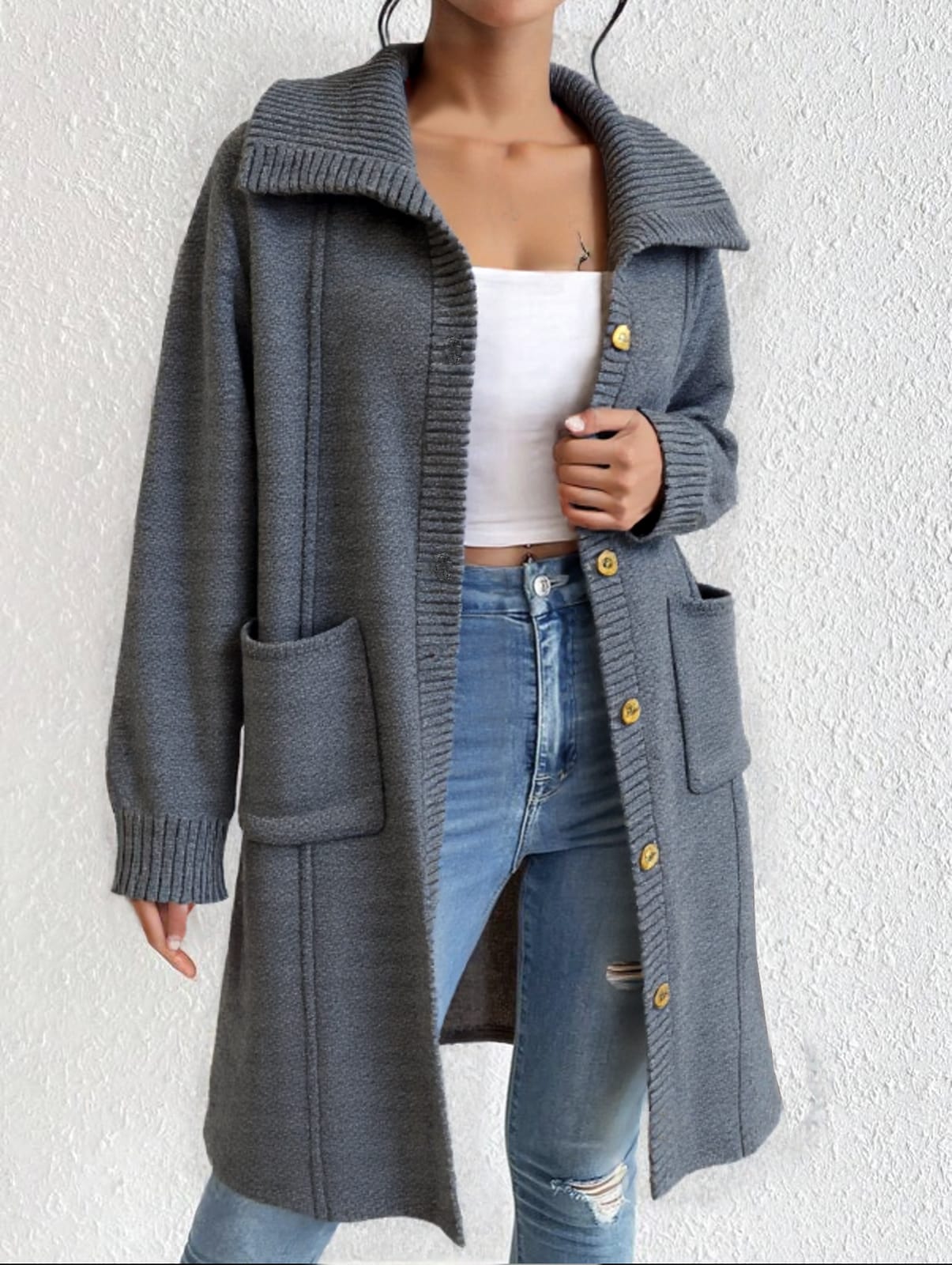 A person is standing against a white wall with their hands in their pockets.