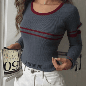 A woman with long brown hair wearing a blue and red striped sweater, white pants, and white shoes.