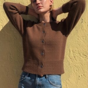 A woman stands confidently against a yellow wall, her body language suggesting she is posing for the photo.