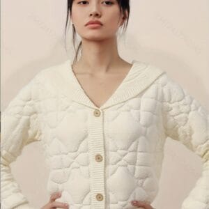 A young woman stands confidently against a light pink background, wearing a white collared shirt with a v-neck and buttons.