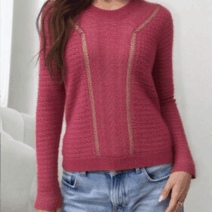 A woman stands confidently with her hands on her hips, wearing a vibrant pink sweater adorned with gold accents and blue.