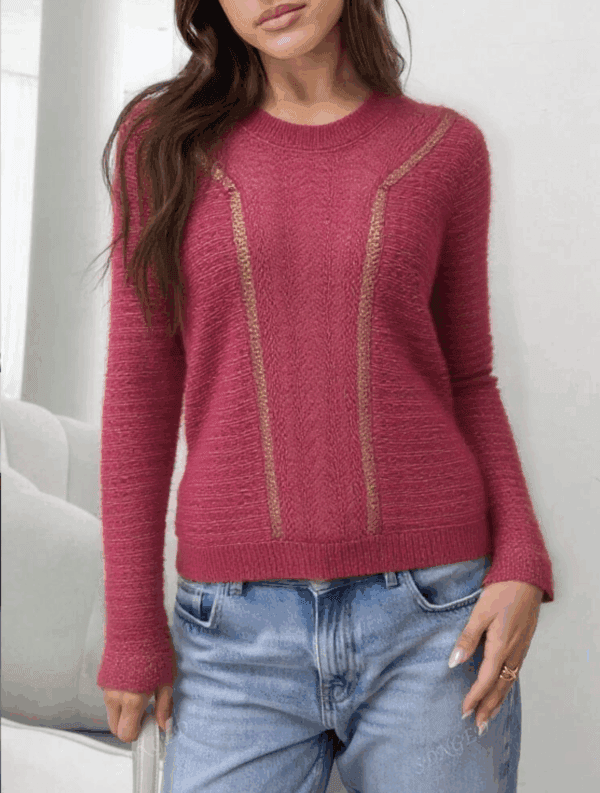 A woman stands confidently with her hands on her hips, wearing a vibrant pink sweater adorned with gold accents and blue.