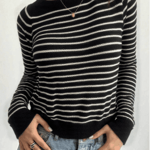 A person stands against a white wall with their hands casually tucked into their pockets and fingers spread apart.