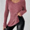 A woman standing against a white background, wearing a pink sweater with an off-the-shoulder neckline and a black skirt.