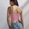 A woman standing against a plain white wall, wearing a pink crop top and blue jeans.